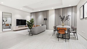 Ein modernes Wohnzimmer mit Sofa, Fernseher, Esstisch und Stühlen.