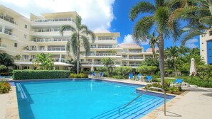 Una piscina con baldosas azules, rodeada de palmeras y sillas de descanso.