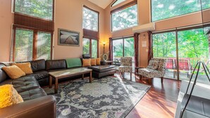 Ein geräumiges Wohnzimmer mit einem großen Ecksofa, einem gemusterten Teppich und Blick ins Freie durch große Fenster.