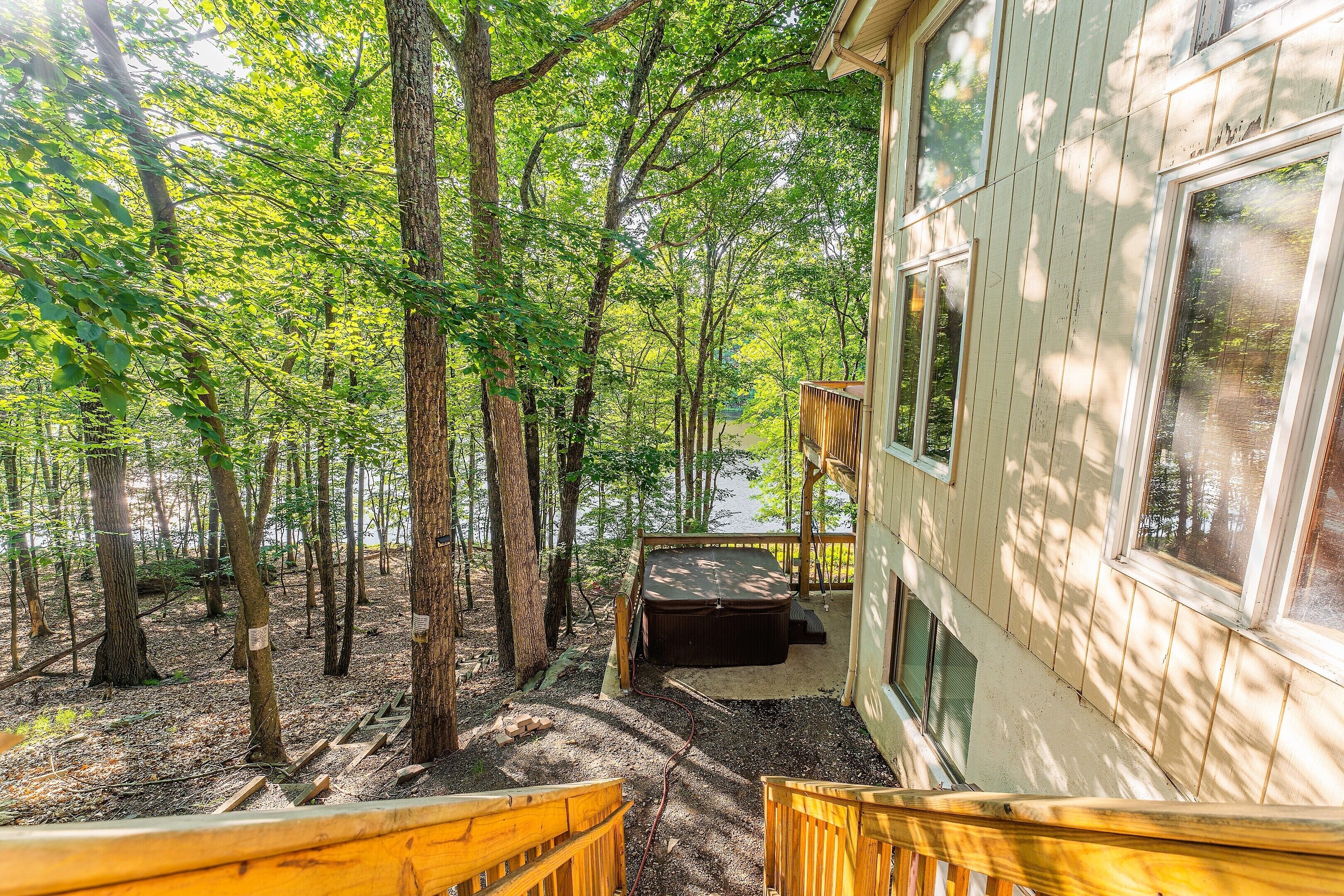 A wooden deck with a hot tub, surrounded by tall trees, leading to a house with large windows.
