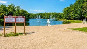 Blick auf einen See mit Sandstrand, einem Rettungsschwimmerstuhl und zwei Informationstafeln.