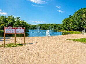 Udsigt over en sø med sandstrand, en livredderstol og to informationsskilte.