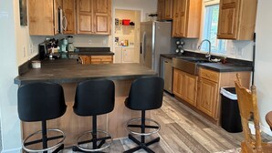 Una cocina moderna con armarios de madera, una isla central con taburetes de bar, electrodomésticos de acero inoxidable e iluminación colgante.