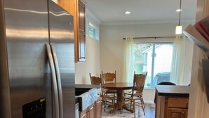 Una cocina moderna con un refrigerador de acero inoxidable, armarios de madera, una mesa de comedor con sillas y una lámpara colgante.