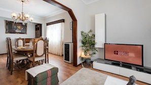 Een moderne woonkamer met een eethoek, een televisie waarop 'GUEST READY' staat en een grote plant.