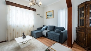 Een woonkamer met een hoekbank, een witte salontafel, een houten kast en een kroonluchter.