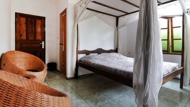 A room with a bed under a canopy, a wicker chair, and a door. - Bagus Bay Homestay (Tuktuk Siadong)