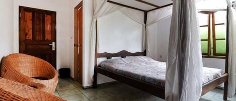 Una habitación con una cama bajo un dosel, una silla de mimbre y una puerta.