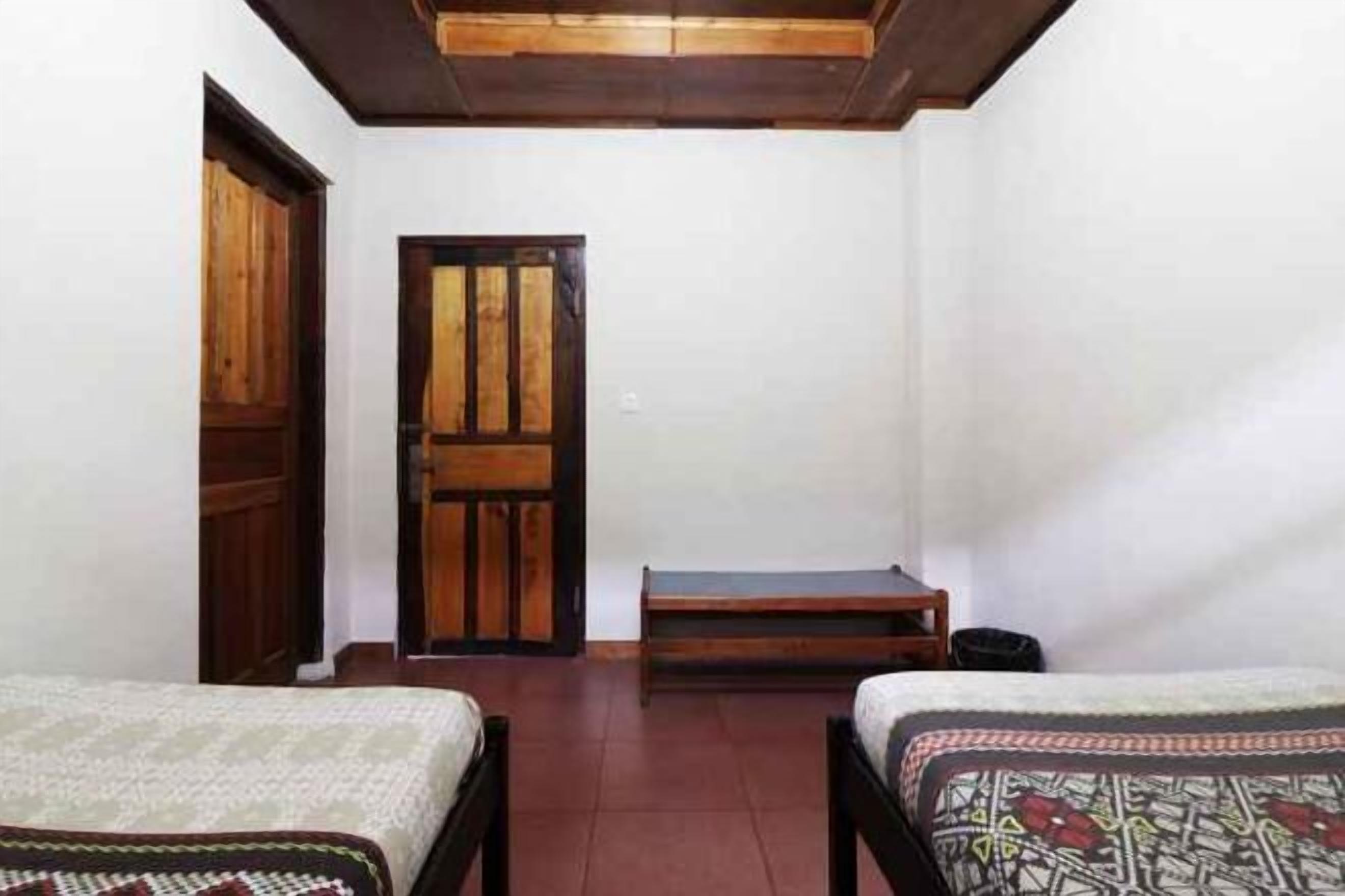 A room with two beds, a wooden door, and a bench.