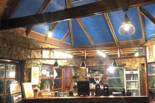 Un interior rústico con techo de madera, paredes de piedra y una zona de bar con mostrador y diversos objetos.