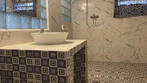 A bathroom with a white sink, patterned tiles, a shower, and a window with patterned curtains. - Bagus Bay Homestay (Tuktuk Siadong)