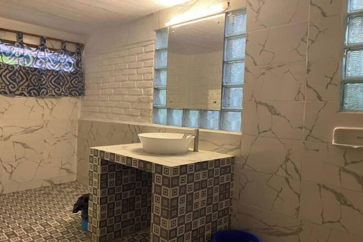 A bathroom with a white sink, patterned tiles, a mirror, and a window with a patterned curtain.
