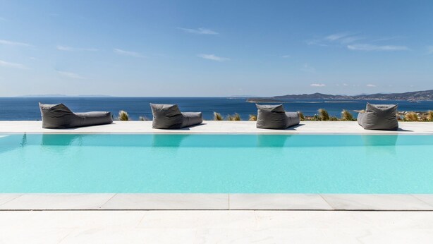 Une piscine avec quatre fauteuils en forme de sac de haricots, disposés face à la mer.