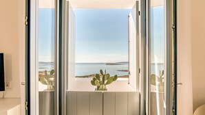 Une pièce dotée d’une grande porte-fenêtre coulissante donnant sur un balcon avec vue sur la mer, et où se trouve un cactus.