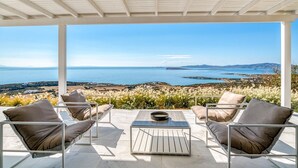 Un espace extérieur abrité, aménagé pour s’asseoir, avec vue sur la mer et les collines.