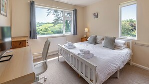Une chambre à coucher comprenant un lit, un bureau, une chaise, un radiateur et deux fenêtres avec des rideaux.