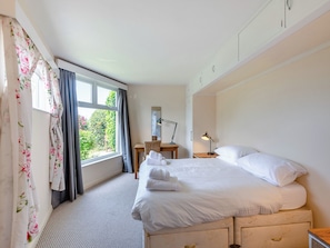 A hotel room with a bed, a desk, a chair, a nightstand, and a window with curtains.