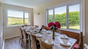 Une salle à manger avec une table dressée pour six personnes, de grandes fenêtres et une vue sur un champ verdoyant.