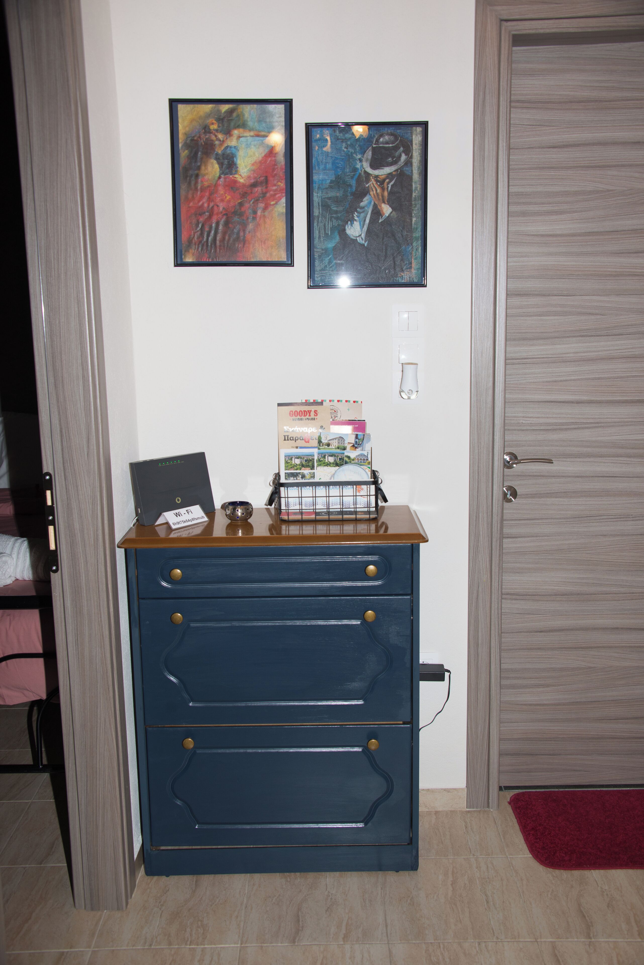Una habitació amb una porta de fusta, un taulell blau amb calaixos, dues obres d'art emmarcades a la paret i una catifa vermella al terra.