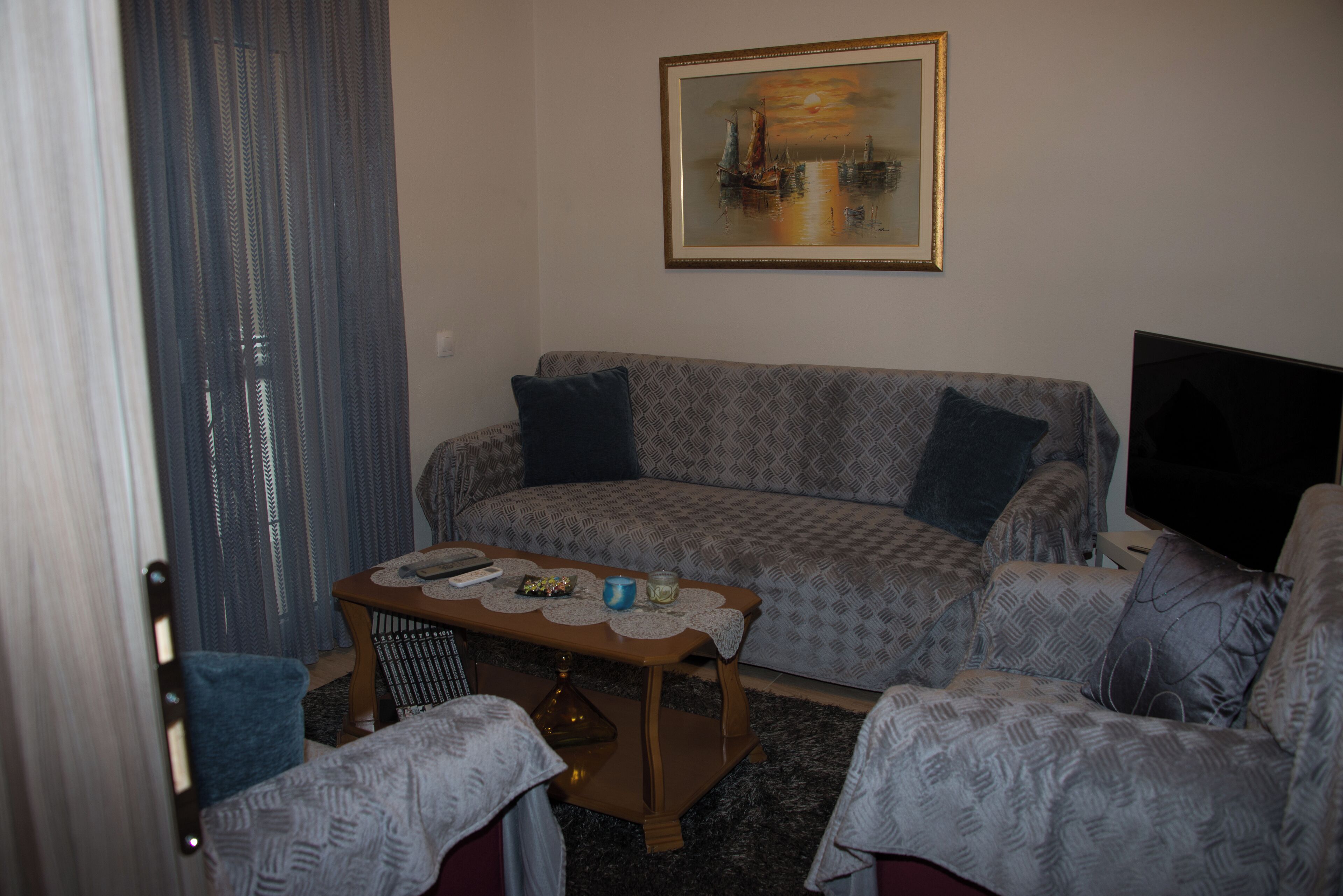 Ein Wohnzimmer mit einem gemusterten Sofa, einem Couchtisch mit Unterlage, einem Fernseher und einem Gemälde an der Wand.