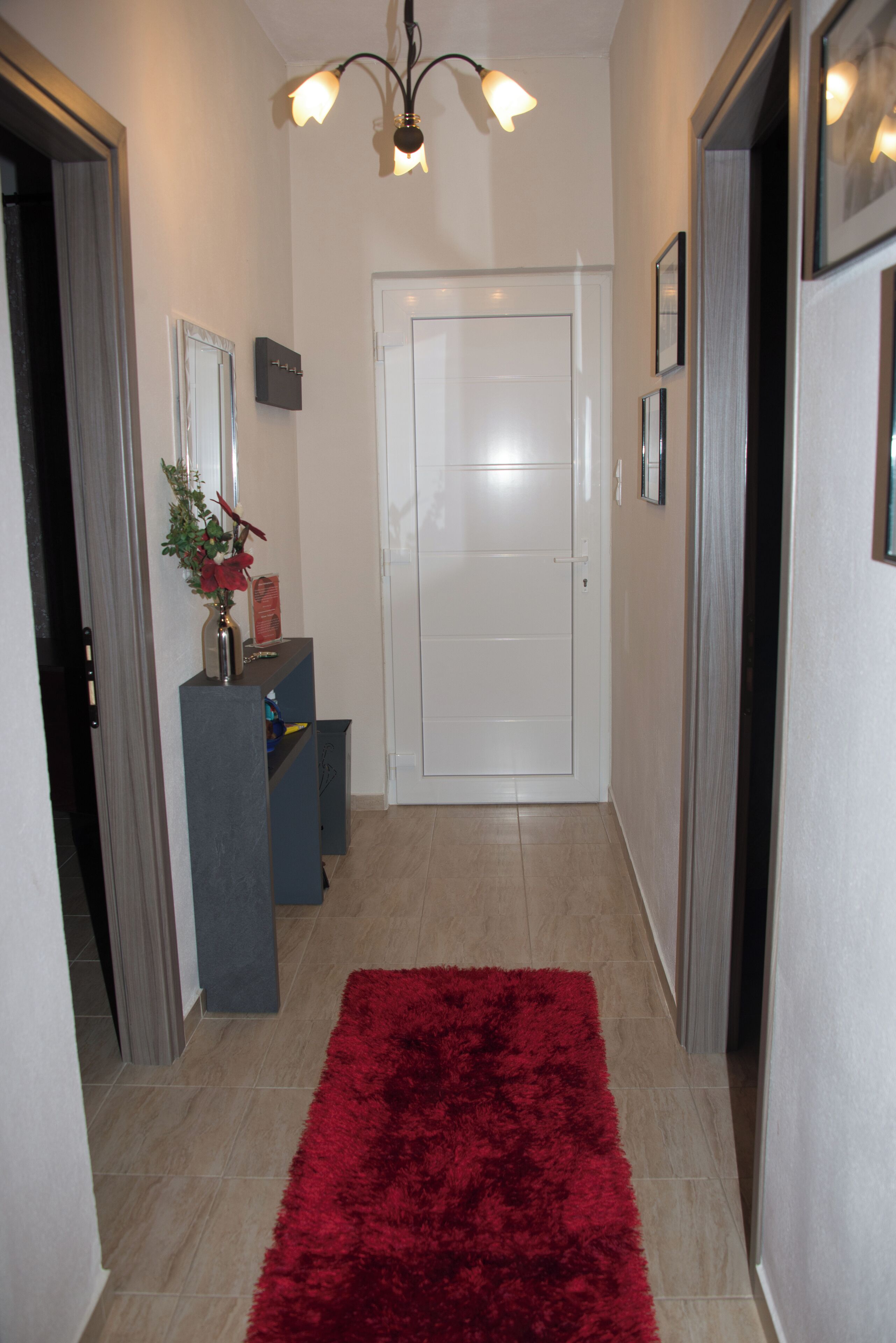 A hallway with a red carpet, a white door, and a small table with a vase and a red box.