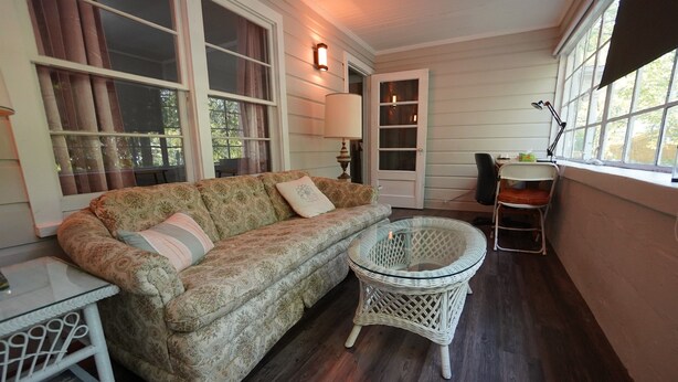 A cozy porch with a patterned sofa, a glass-top table, and a wicker chair. - Pine Haven - Large Group - Baby & Pet friendly (Birmingham)