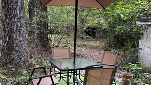 A patio table and chairs with a large umbrella, surrounded by trees and greenery. - Pine Haven - Large Group - Baby & Pet friendly (Birmingham)
