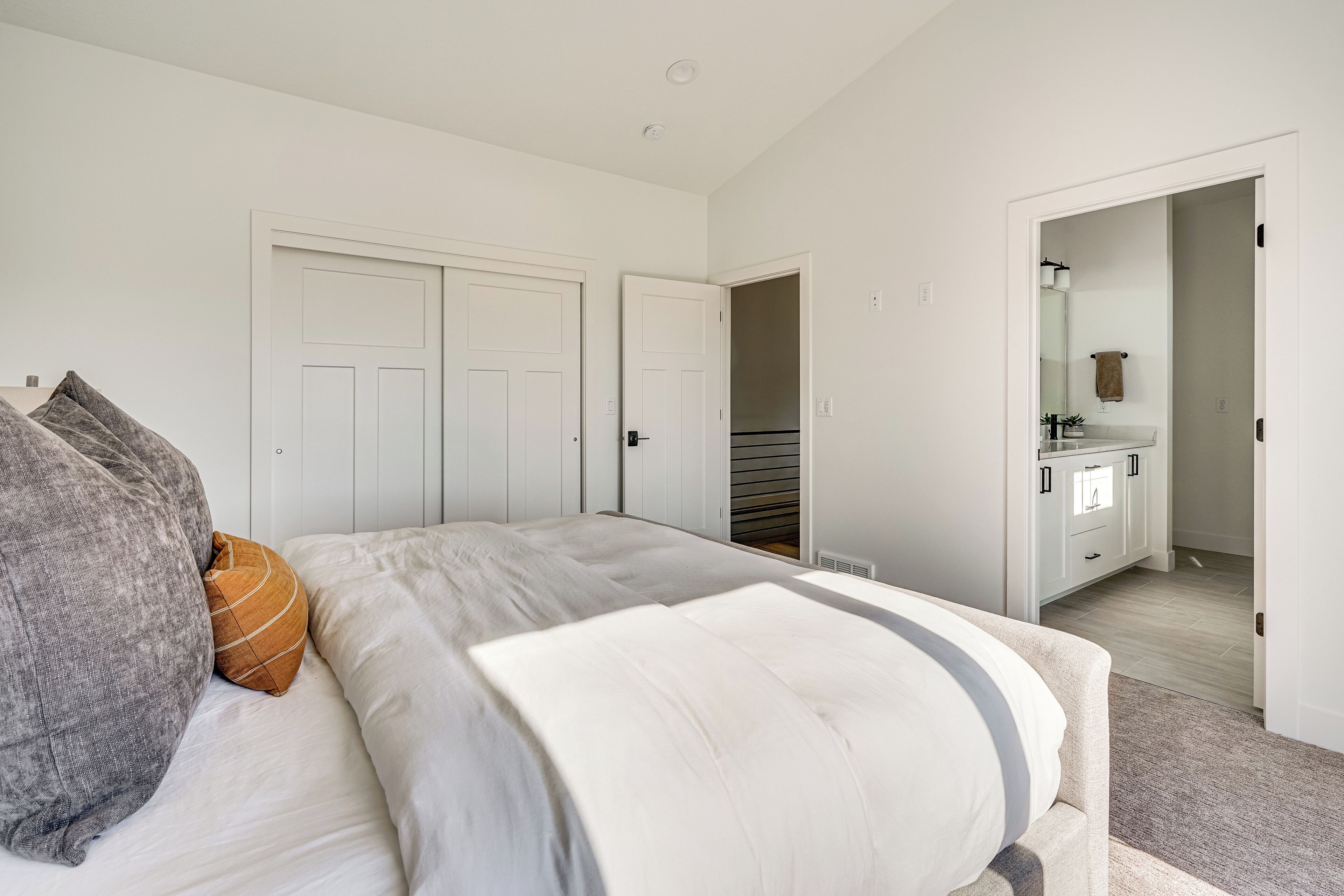 Ein Schlafzimmer mit einem Bett, weißen Wänden, einem Kleiderschrank und einem durch eine offene Tür einsehbaren Badezimmer.
