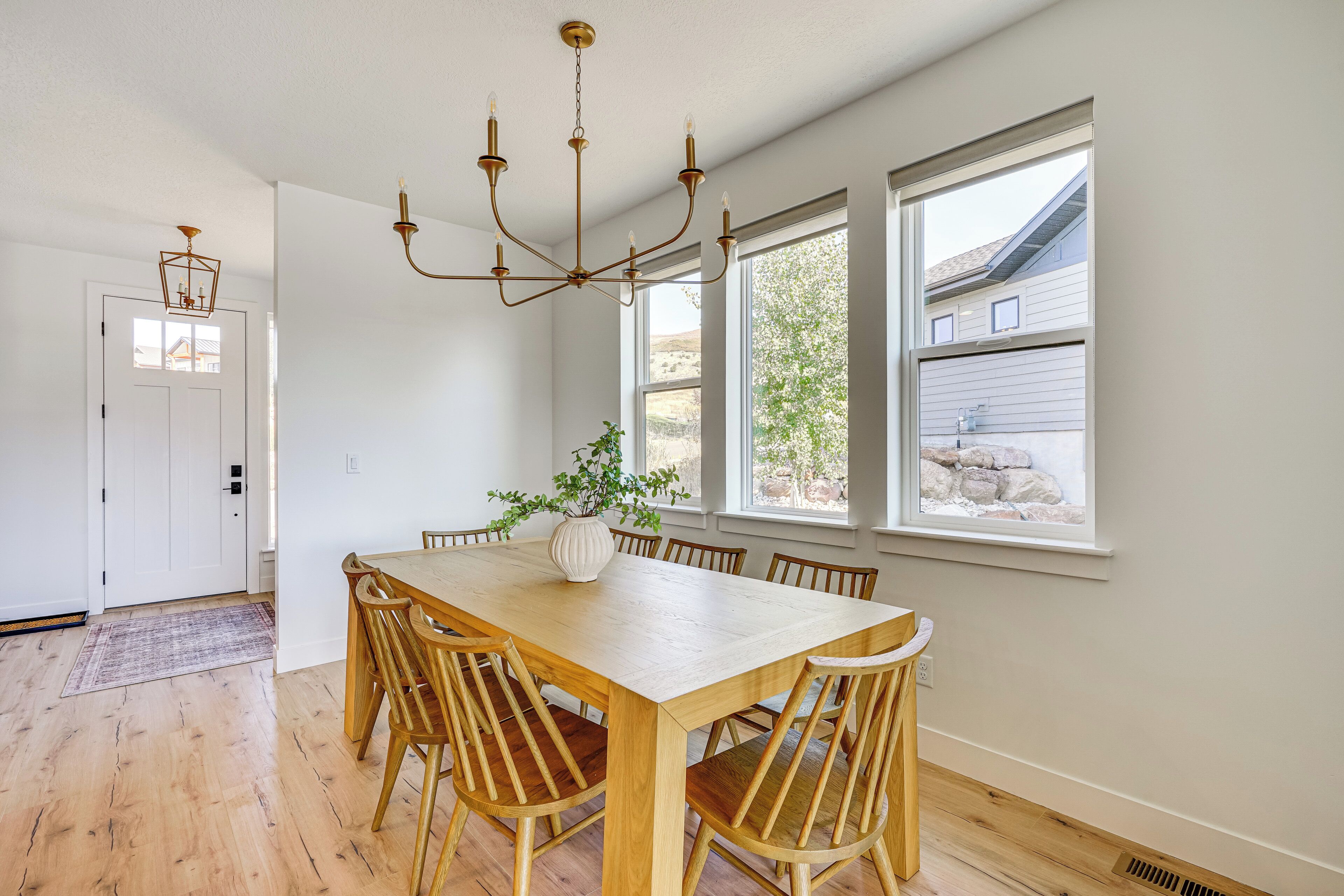 A dining area with a wooden table and chairs, a chandelier, and a potted plant.
