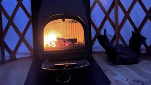 Una estufa de leña con fuego encendido, frente a un muro de celosía.