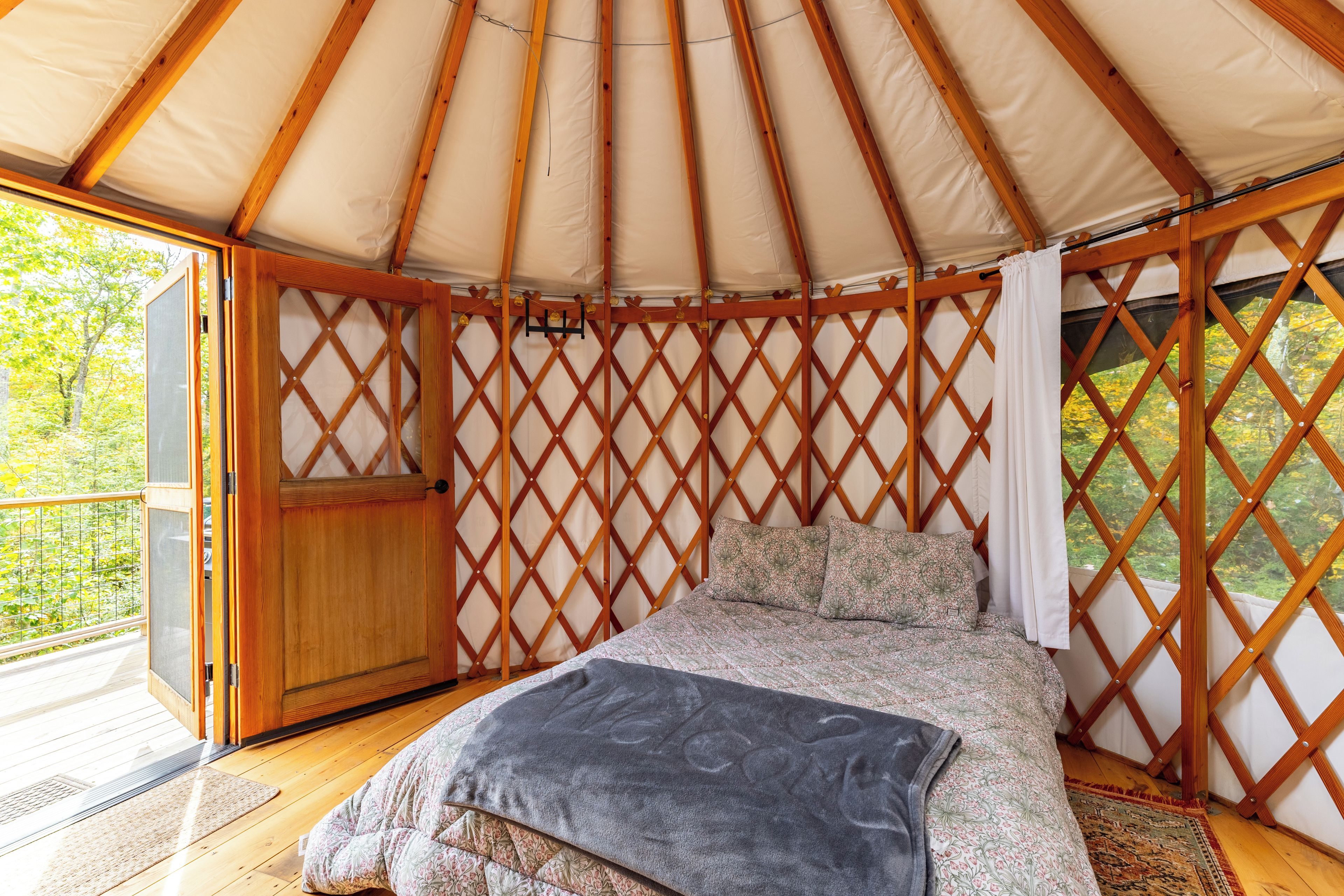 Interior de una yurta con cama, paredes de celosía de madera y una puerta.