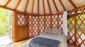 Interior de una yurta con cama, paredes de celosía de madera y una puerta.