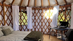 Una carpa acogedora con una cama, una mesita con una computadora portátil y vistas a la vegetación.