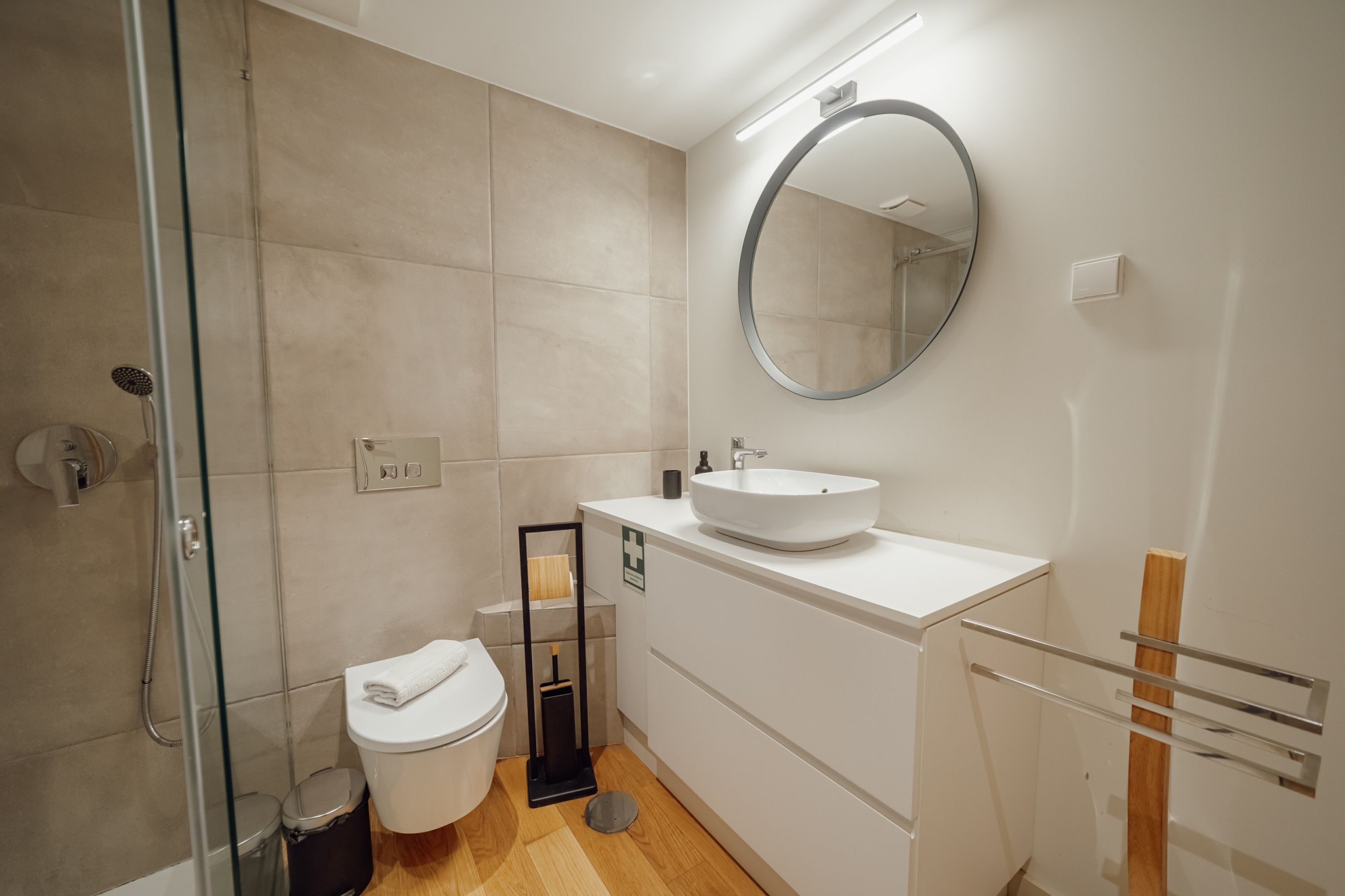 A modern bathroom with a glass-enclosed shower, a white toilet, a sink with a mirror above it, and a towel rack.