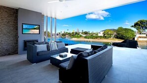 A modern living room with a large window overlooking a pool and a cityscape. - Luxico Bluewater Oasis (Heated Pool) (Broadbeach Waters)
