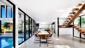 A modern interior with a dining area, a pool, and a staircase. - Luxico Bluewater Oasis (Heated Pool) (Broadbeach Waters)
