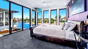 A bedroom with a large bed, a ceiling fan, and a view of a body of water through large windows. - Luxico Bluewater Oasis (Heated Pool) (Broadbeach Waters)