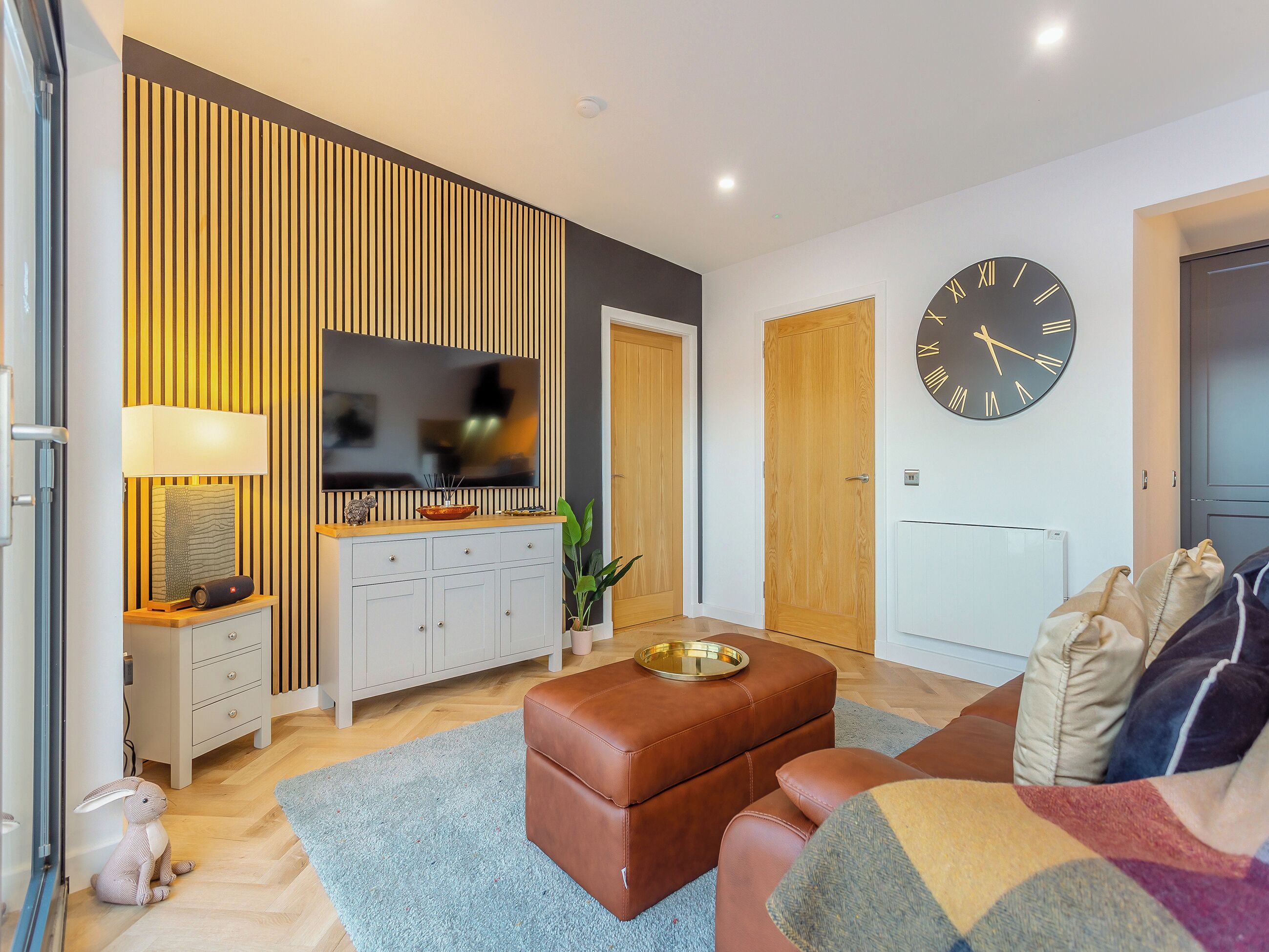 A modern living room with a flat-screen TV, a large clock, and a cozy seating area.
