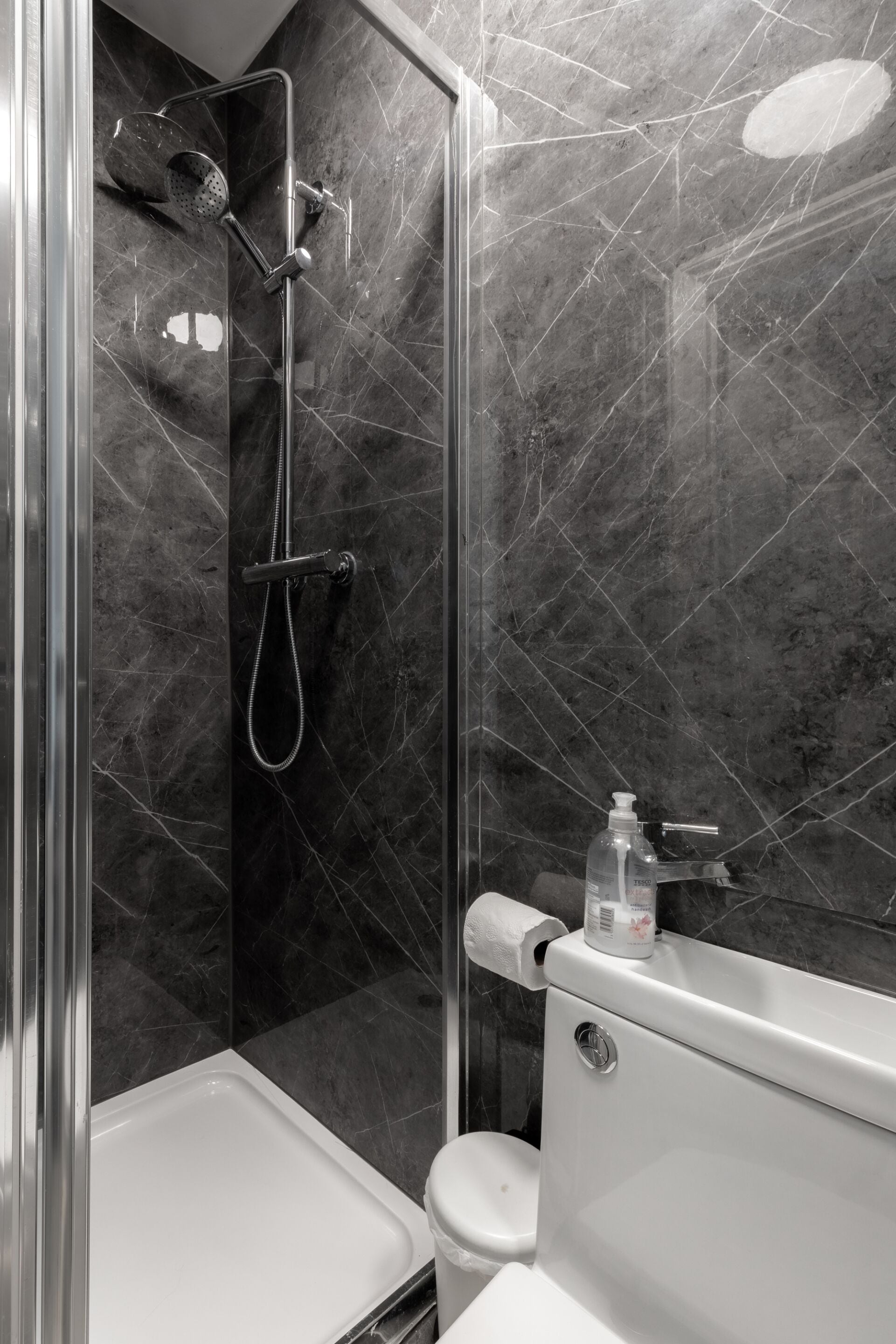 Een moderne badkamer met een douche met glazen wand, een toilet en een wastafel met zeepdispenser.