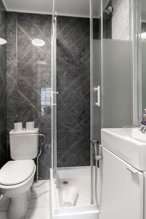 A modern bathroom with a glass-enclosed shower, a toilet, and a sink. - The Savers Hotel by PLI (London)