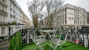 Ein Balkon mit einem grünen Rasen, Metallstühlen und einem Tisch.