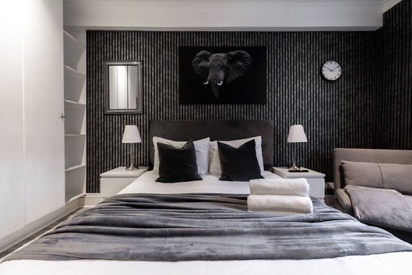A modern bedroom with a large bed, a headboard with an elephant head, a clock, and a mirror on the wall. - The Savers Hotel by PLI (London)