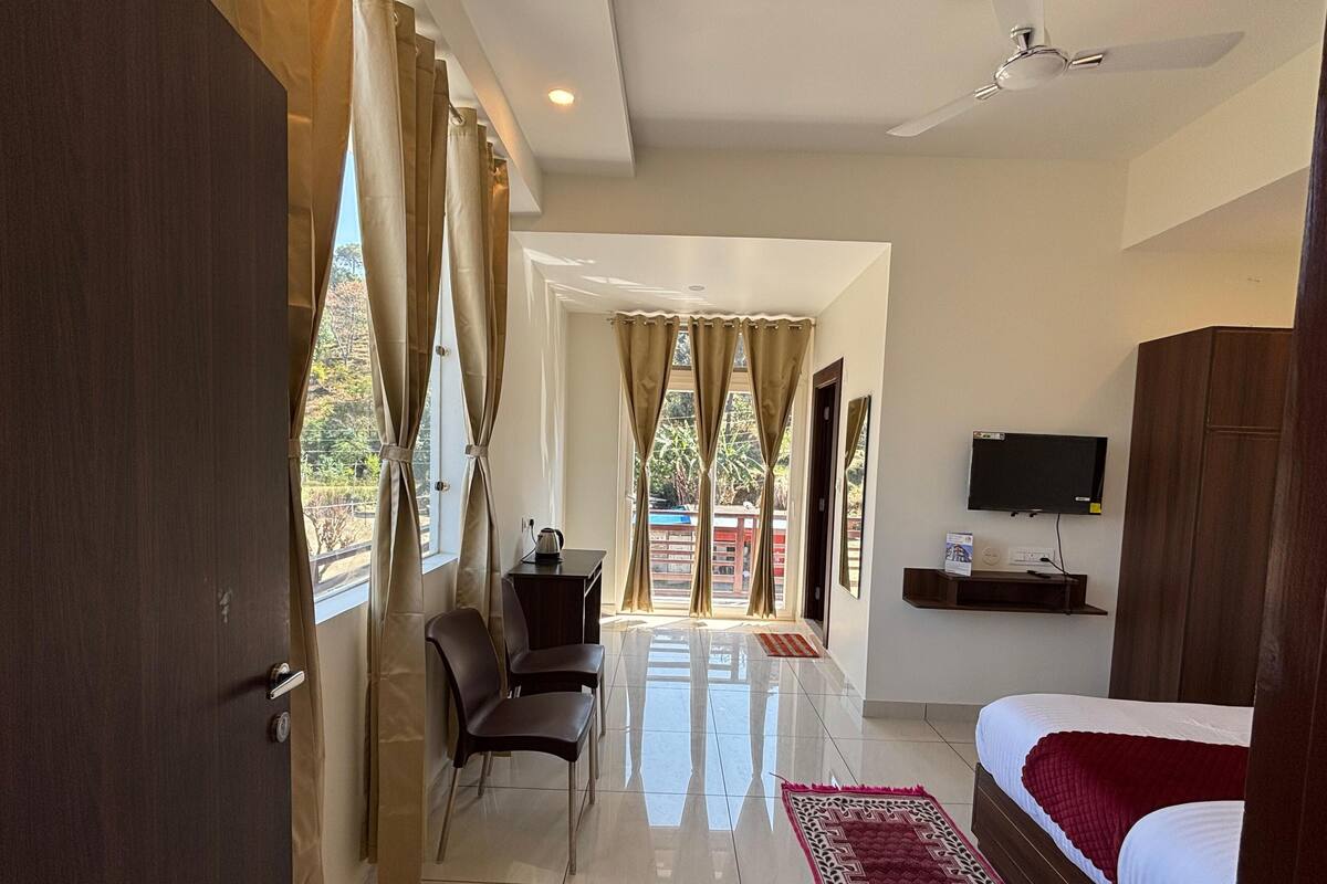 A hotel room with a bed, a TV, a desk with a chair, and a view of the outside.