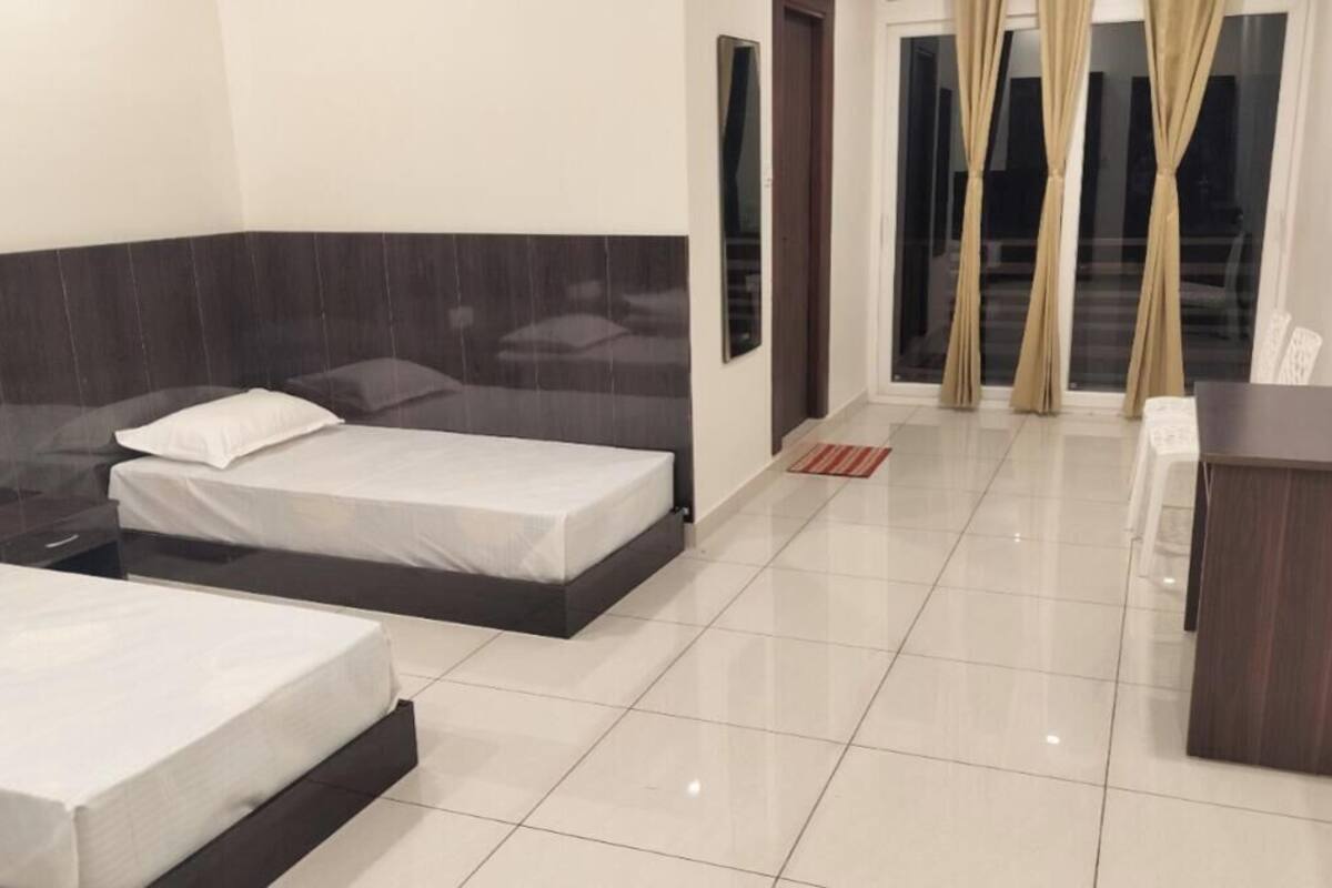 A hotel room with two beds, a desk, and a view of the outside through a window with curtains.