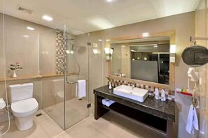 A modern bathroom with a glass shower enclosure, a white toilet, a sink with a mirror, and a towel rack. - Travello Hotel Bandung (Cidadap)