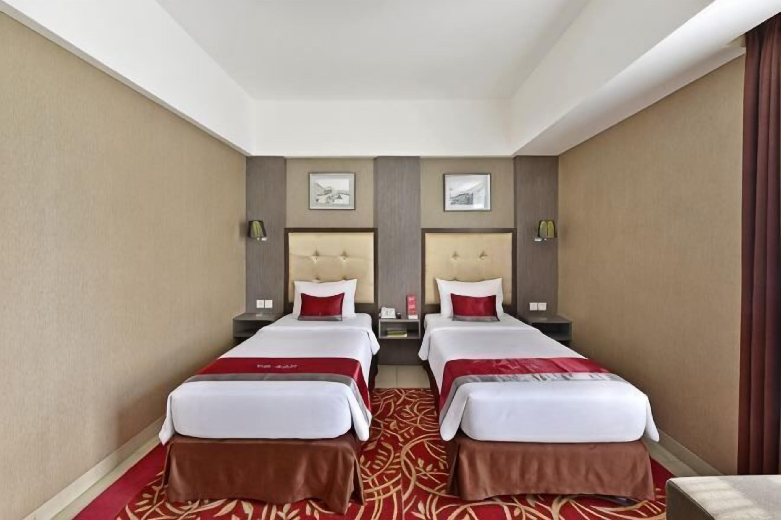 Une chambre d’hôtel avec deux lits, une moquette rouge et une vue sur la ville.