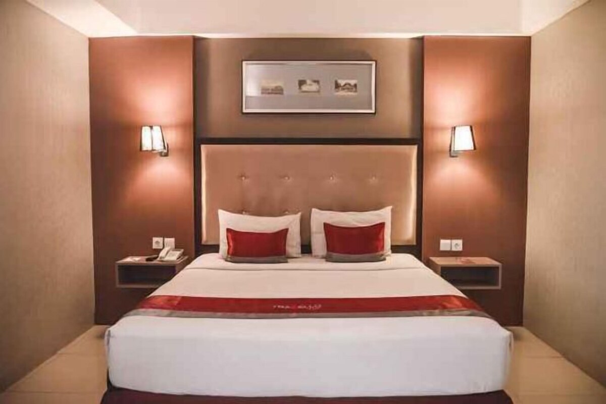 A hotel room with a large bed, two bedside tables, and wall-mounted lamps.