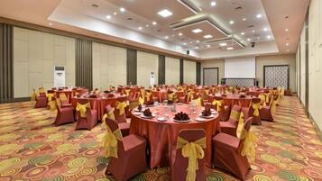 A large banquet hall with round tables and chairs, carpeted floor, and a high ceiling with recessed lighting.