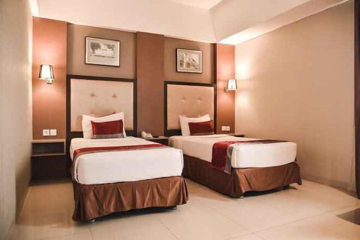 A hotel room with two beds, a nightstand, a lamp, and a framed picture on the wall.