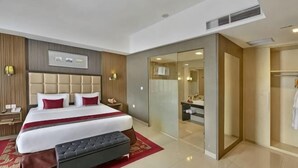 Ein modernes Hotelzimmer mit einem großen Bett, Nachttischen, einer Bank, einer Schiebetür zum Badezimmer und einem Spiegel.